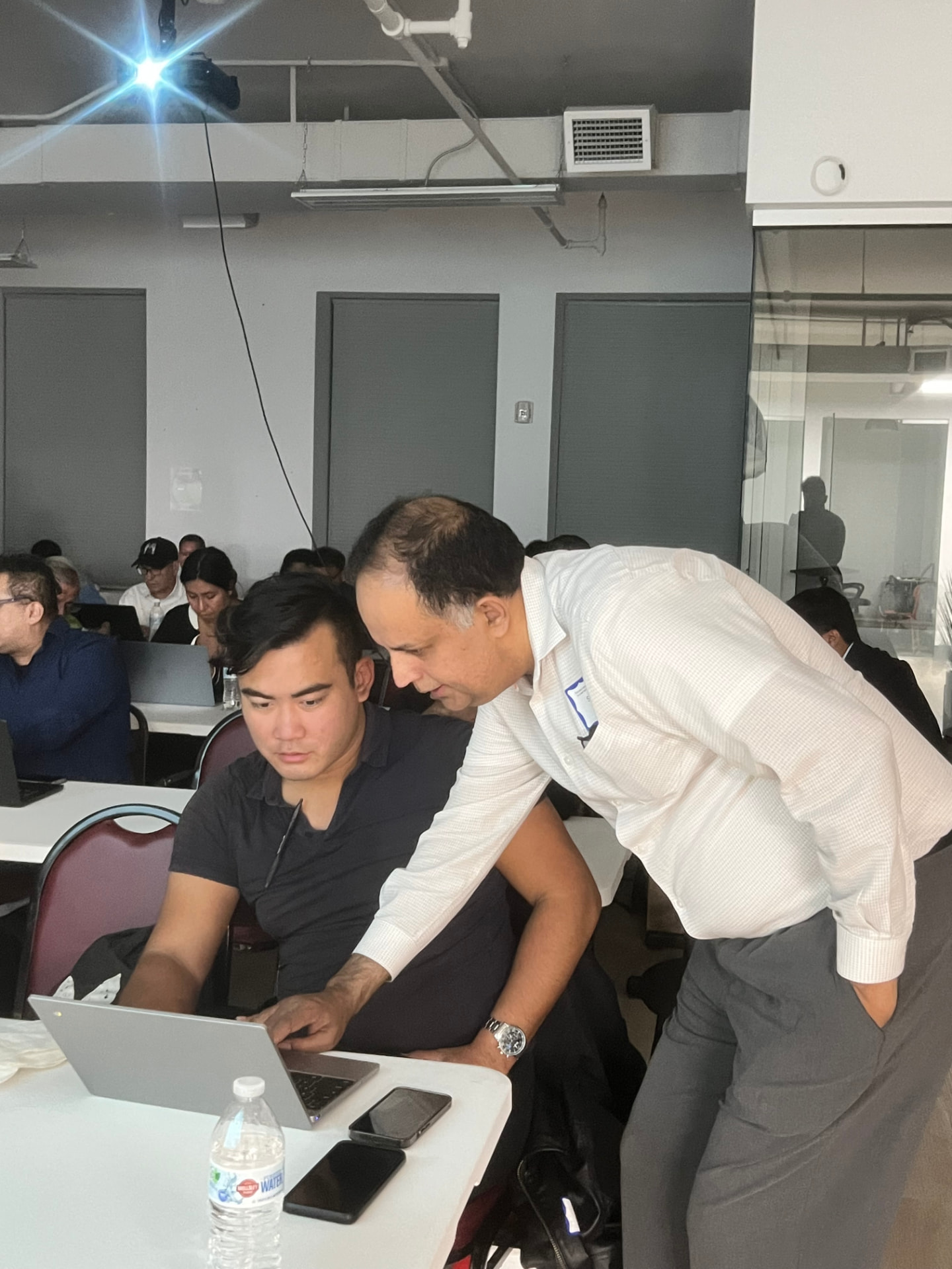 A teacher leaning over to help an attendee at their laptop during class