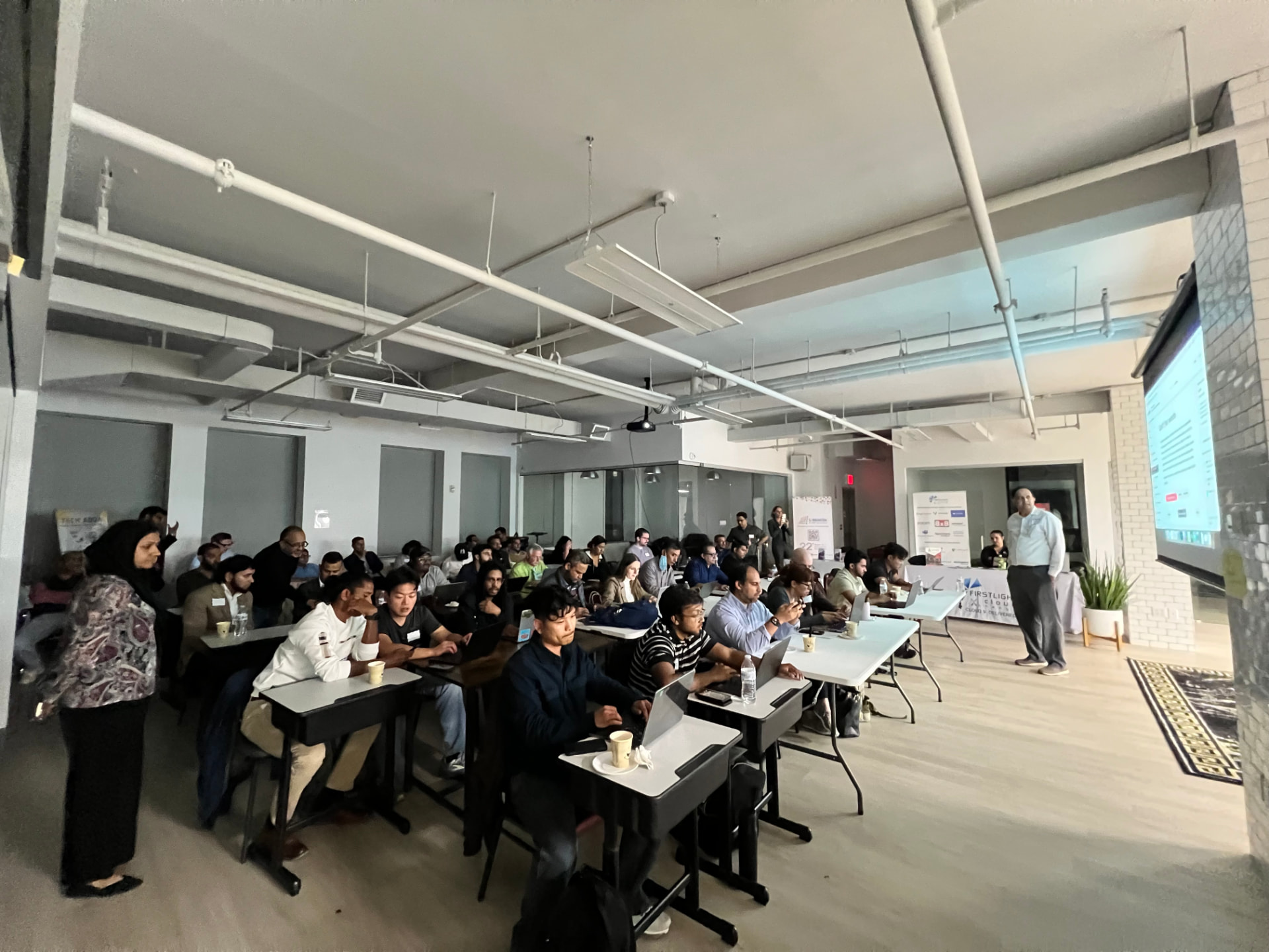A teacher presenting to a full room of attendees working on laptops at an AI class